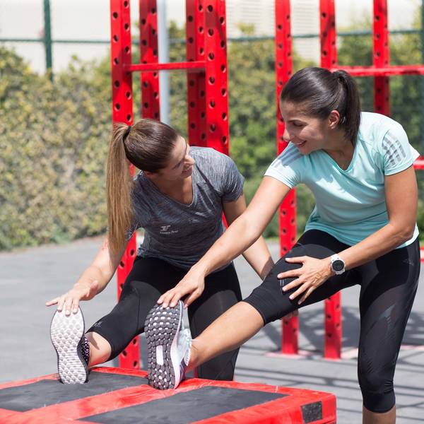two female Fitness First members stretching in outdoor workout space two female Fitness First members stretching in outdoor workout space